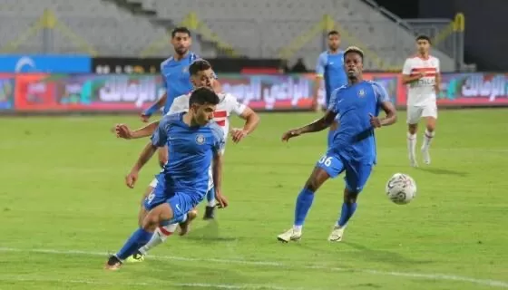 Joueurs en bleu et en blanc-rouge en plein match de football avec ballon au sol sur le terrain vert