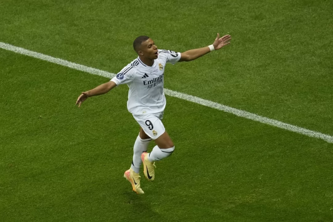Un joueur de football en maillot blanc célèbre un but sur un terrain vert près de la ligne de touche