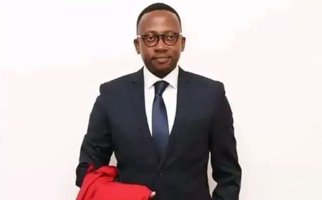 Homme en costume sombre et cravate tenant une veste rouge devant un mur blanc