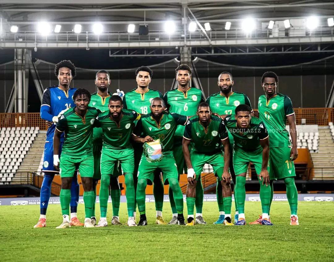 Onze joueurs de football en tenue verte posant sur un terrain de stade vide sous des projecteurs allumés