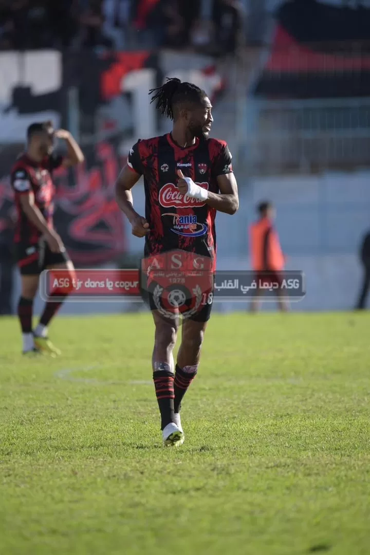 Un joueur de football en tenue rouge et noire court sur le terrain en regardant sur le côté