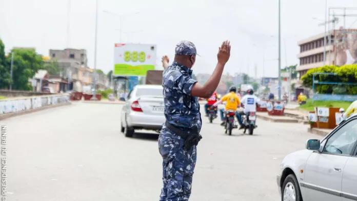 Un policier en uniforme bleu arrête la circulation d'une voiture blanche sur une route urbaine animée