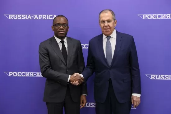 Deux hommes en costume cravate se serrent la main devant un fond bleu avec inscriptions « RUSSIA-AFRICA » et écriture en cyrillique