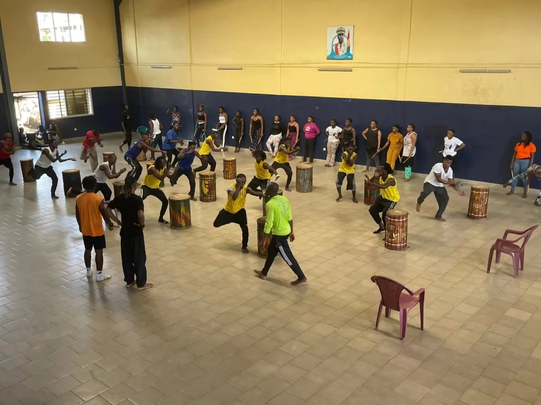 Jeunes en tenue de sport dans une salle effectuent une danse rythmée autour de djembés disposés en cercle