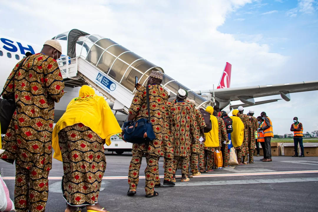Des passagers habillés en tenues traditionnelles font la queue pour embarquer dans un avion au sol sur un aéroport