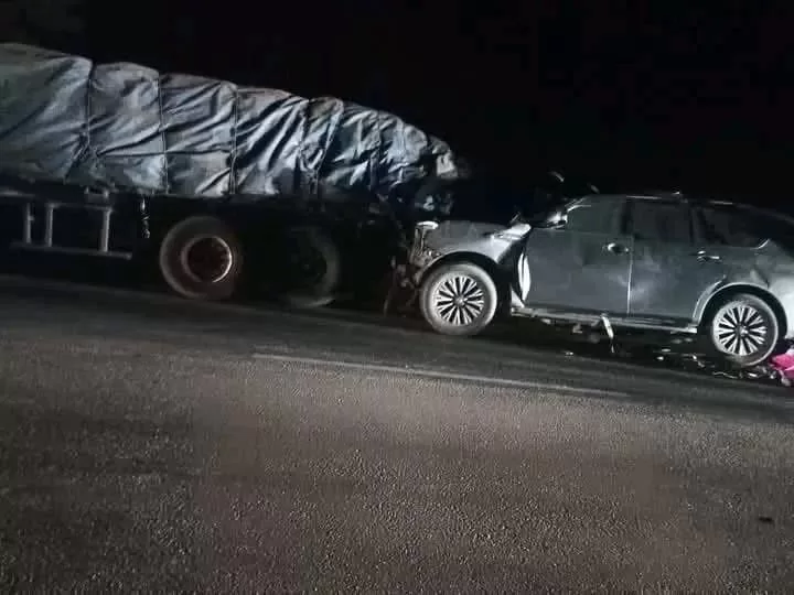 Une voiture SUV endommagée est encastrée à l'avant dans un poids lourd arrêté sur une route de nuit