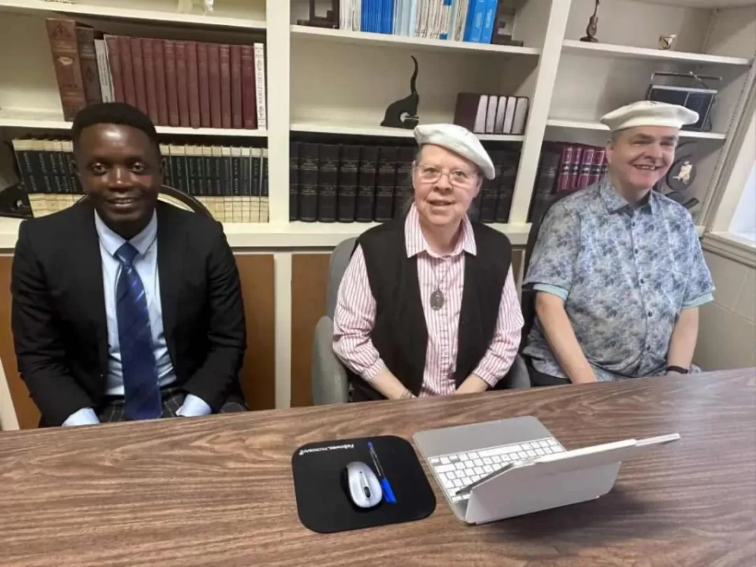 Trois personnes assises devant une table avec un ordinateur, une étagère remplie de livres en arrière-plan