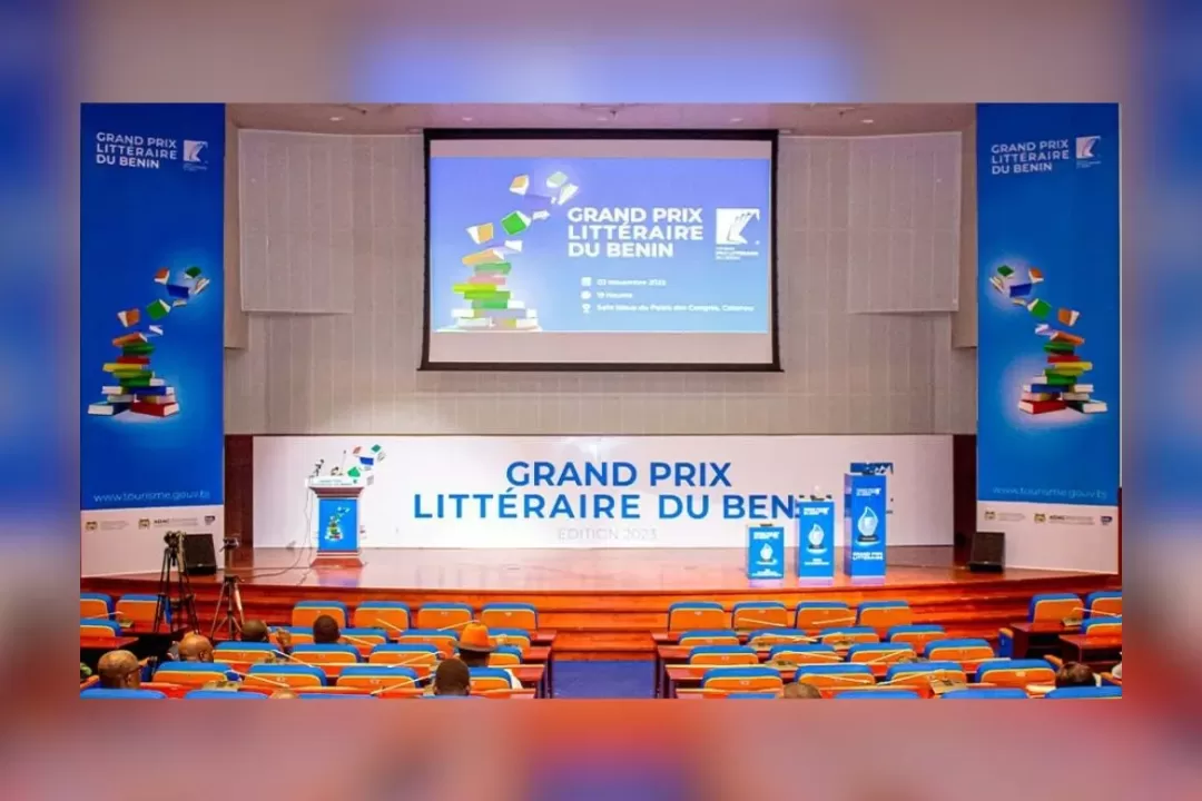 Salle de conférence avec des sièges bleus et une scène ornée de bannières du Grand Prix Littéraire du Bénin
