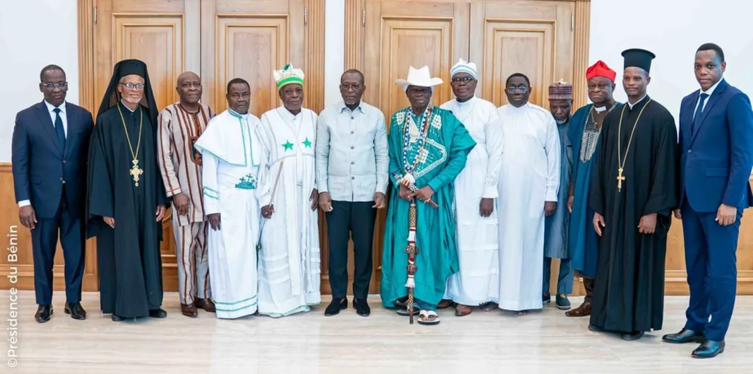 Groupe d’hommes en vêtements traditionnels et religieux posant dans une salle avec un sol en marbre et des portes en bois claires