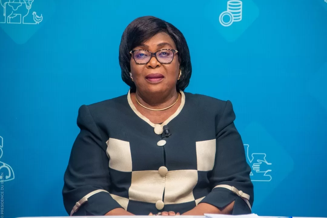 Femme assise devant un fond bleu décoré d’icônes blanches, portant une veste noire et crème et des lunettes