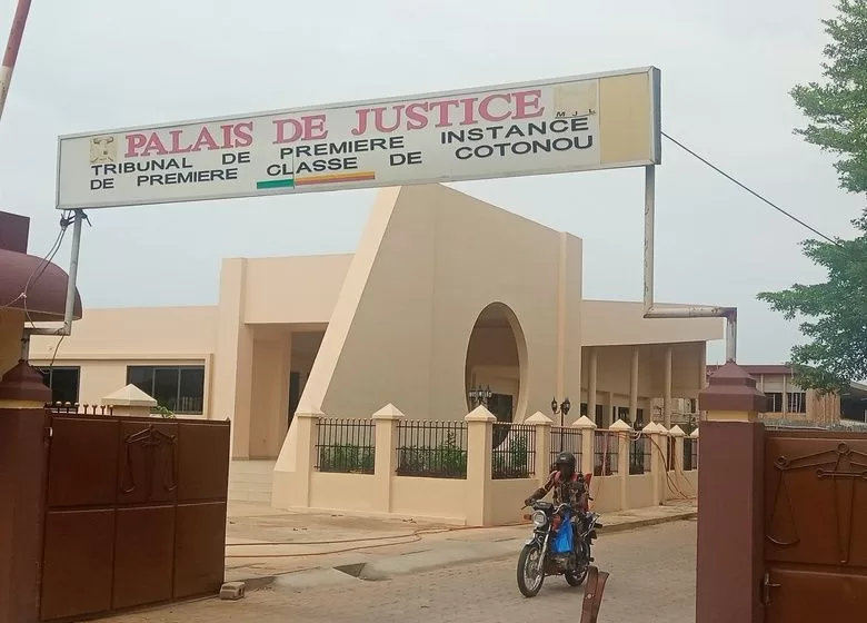 Façade d un bâtiment avec un panneau intitulé Palais de Justice Tribunal de Première Instance Classe de Cotonou et un homme à moto devant