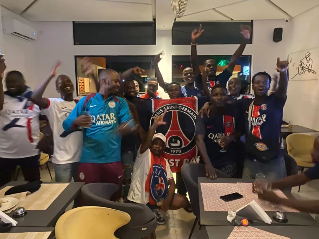 Groupe d'hommes célébrant avec un drapeau Paris Saint-Germain dans une salle avec tables et chaises