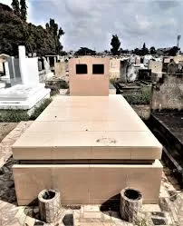 Tombe en pierre claire entourée d'autres sépultures dans un cimetière sous un ciel nuageux