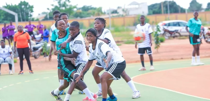 Jeunes joueuses en maillots blancs et verts s'affrontent sur un terrain de handball en plein air lors d'un match intense