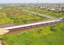 Vue aérienne d'une large zone verte avec une infrastructure linéaire bordée d'eau et des constructions en arrière-plan