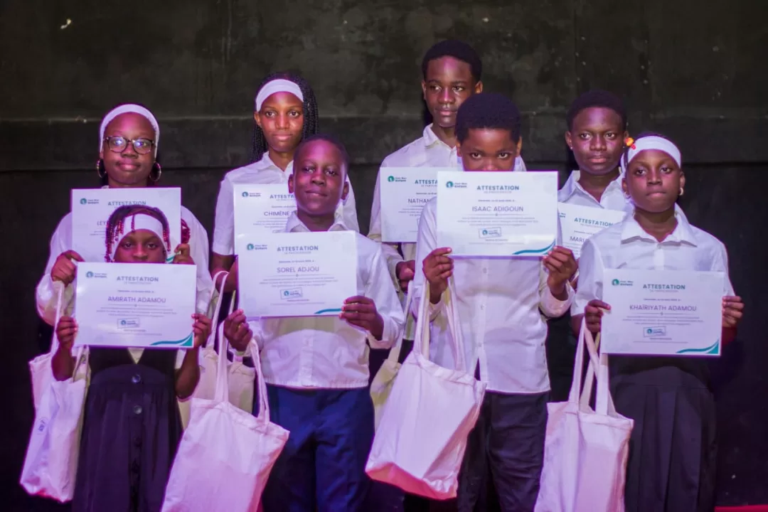 Huit enfants vêtus de blanc tiennent des attestations et des sacs en tissu devant un fond sombre