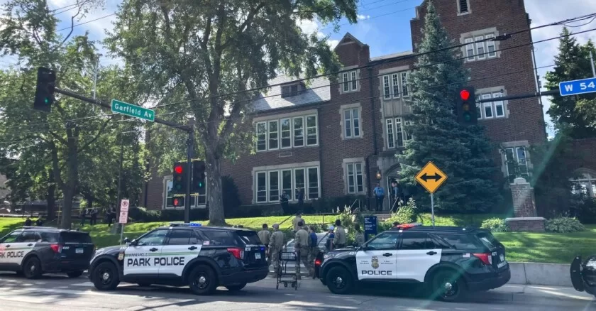 Plusieurs véhicules de police stationnés devant un bâtiment en pierre avec des personnes rassemblées sur le trottoir