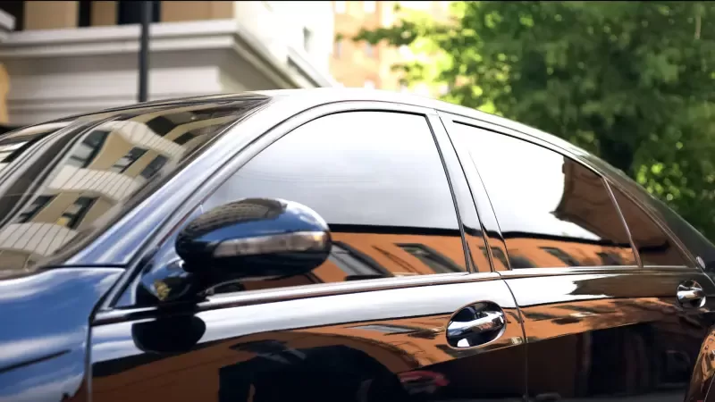 Voiture noire aux vitres fortement teintées reflétant bâtiments et arbres au soleil