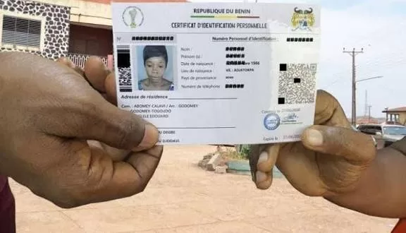 Deux mains tiennent un certificat d'identification personnelle devant une rue avec quelques bâtiments en arrière-plan