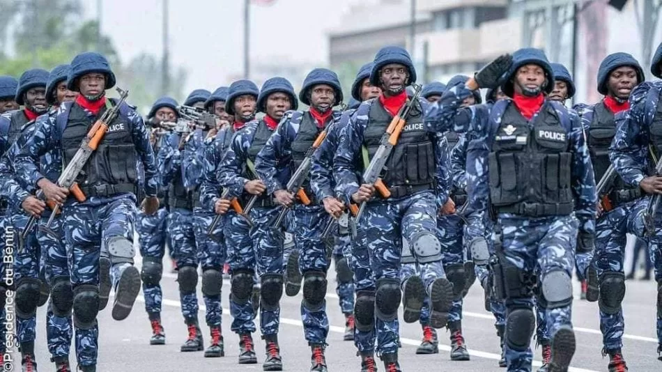 Un groupe de policiers en uniforme bleu camouflage défile en formation serrée sur une avenue urbaine