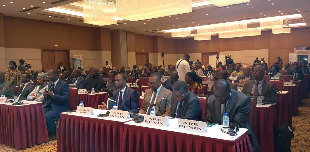 Un groupe de personnes assises dans une salle de conférence avec des tables couvertes de nappes rouges et un public en arrière-plan