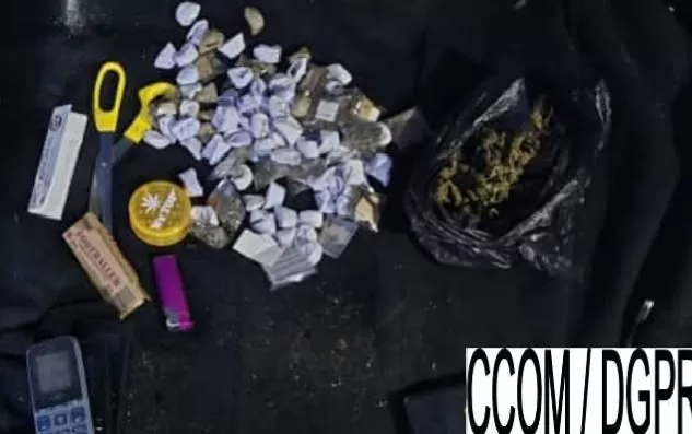 Plusieurs sachets transparents contenant une substance verte, un briquet violet, un cutter jaune, un grinder jaune et un téléphone posés sur un tissu noir.