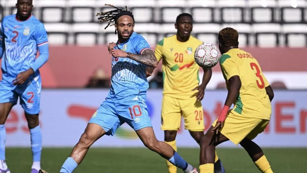 Un joueur en maillot bleu contrôle le ballon face à deux adversaires en maillots jaunes sur un terrain de football