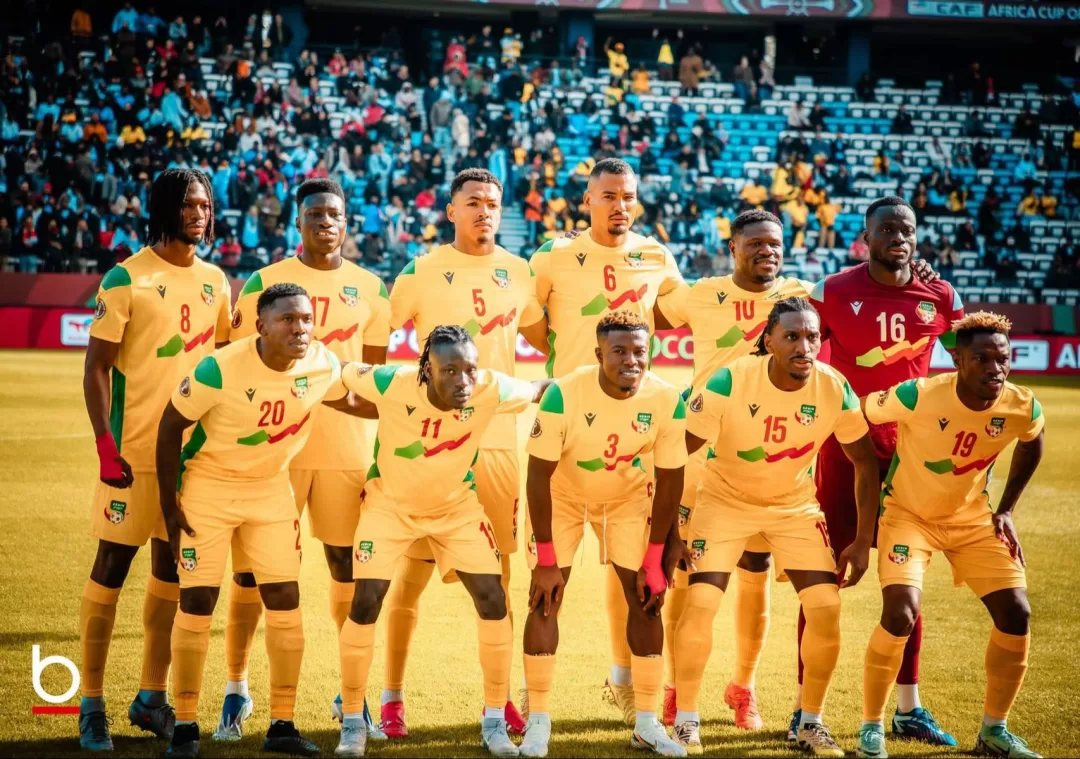 Onze joueurs en tenue de football jaune posent sur un terrain avec un public en tribunes en arrière-plan