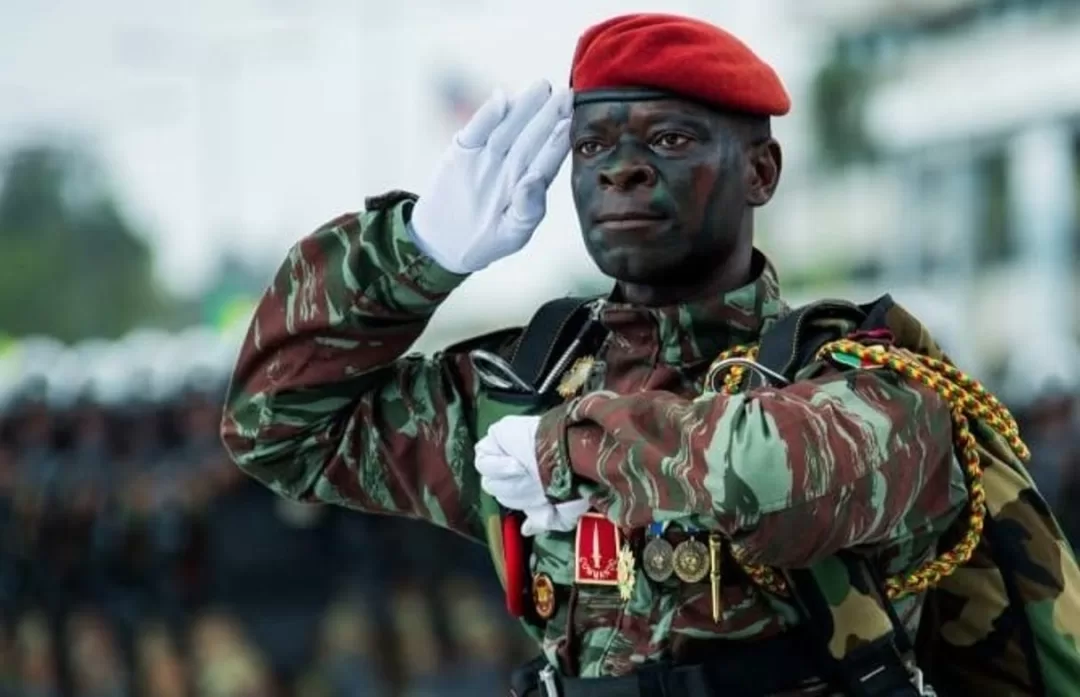Un militaire en uniforme de camouflage et béret rouge effectue un salut solennel lors d'une cérémonie militaire en extérieur