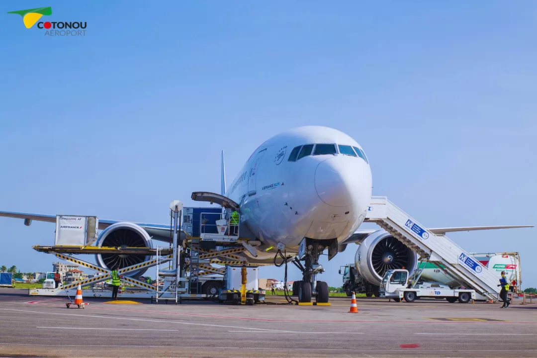 Un avion stationné sur le tarmac avec plusieurs équipements de chargement et du personnel autour sous un ciel bleu clair