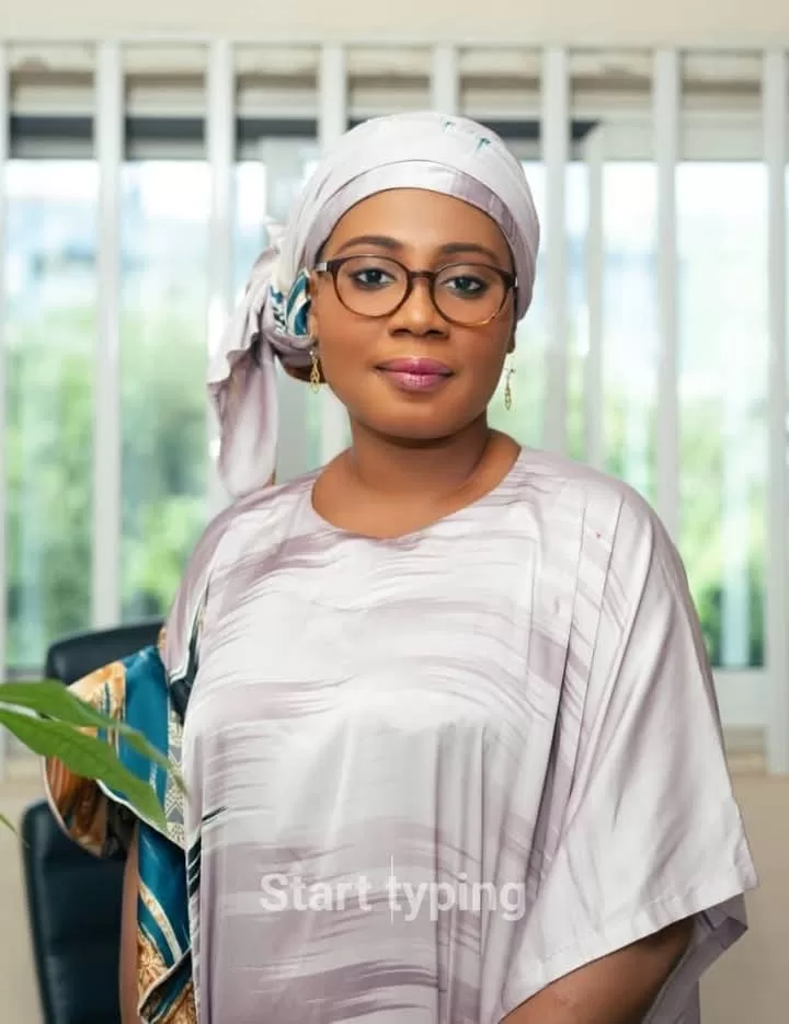 Femme portant un foulard et des lunettes posant devant une fenêtre lumineuse dans une pièce intérieure