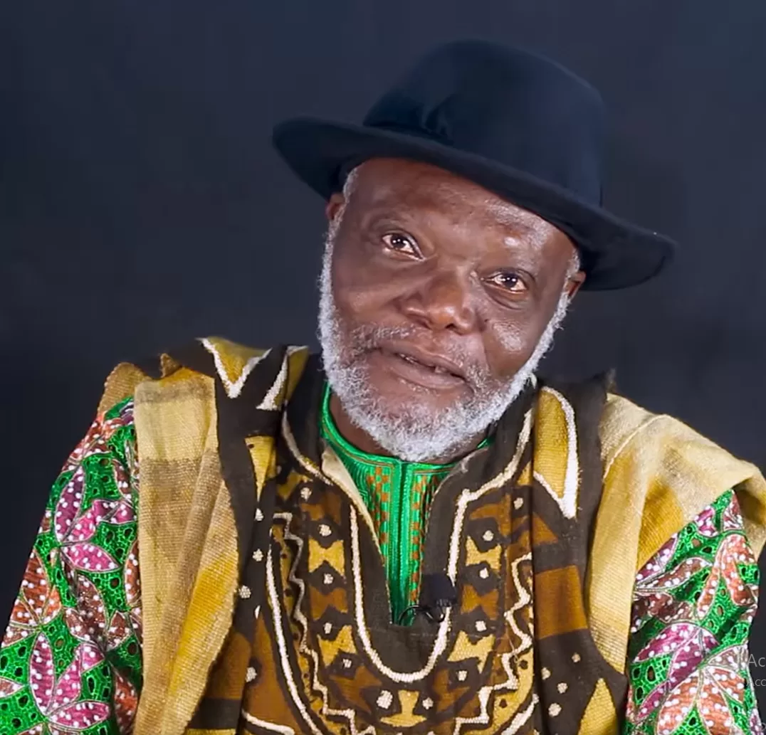 Homme âgé portant un chapeau noir et un vêtement coloré traditionnel africain sur fond sombre