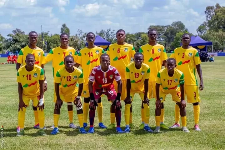 Onze jeunes joueurs de football en tenue jaune et verte posent sur un terrain herbeux sous un ciel partiellement nuageux