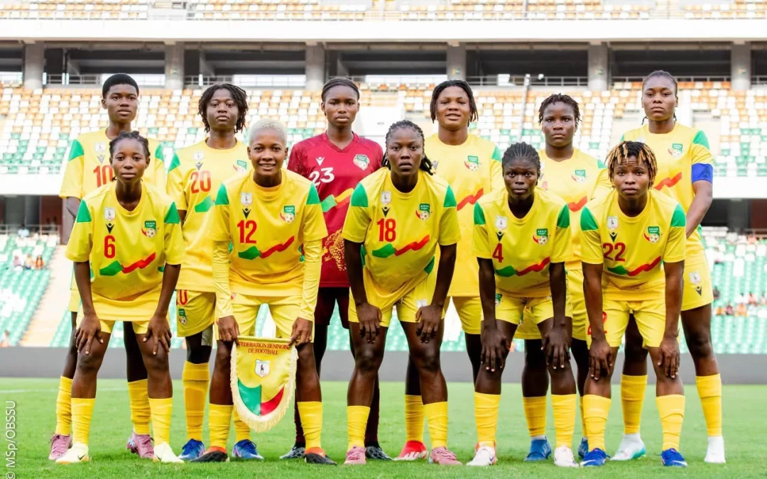 Onze joueuses en tenue jaune posent en rang devant les gradins d’un stade de football vide
