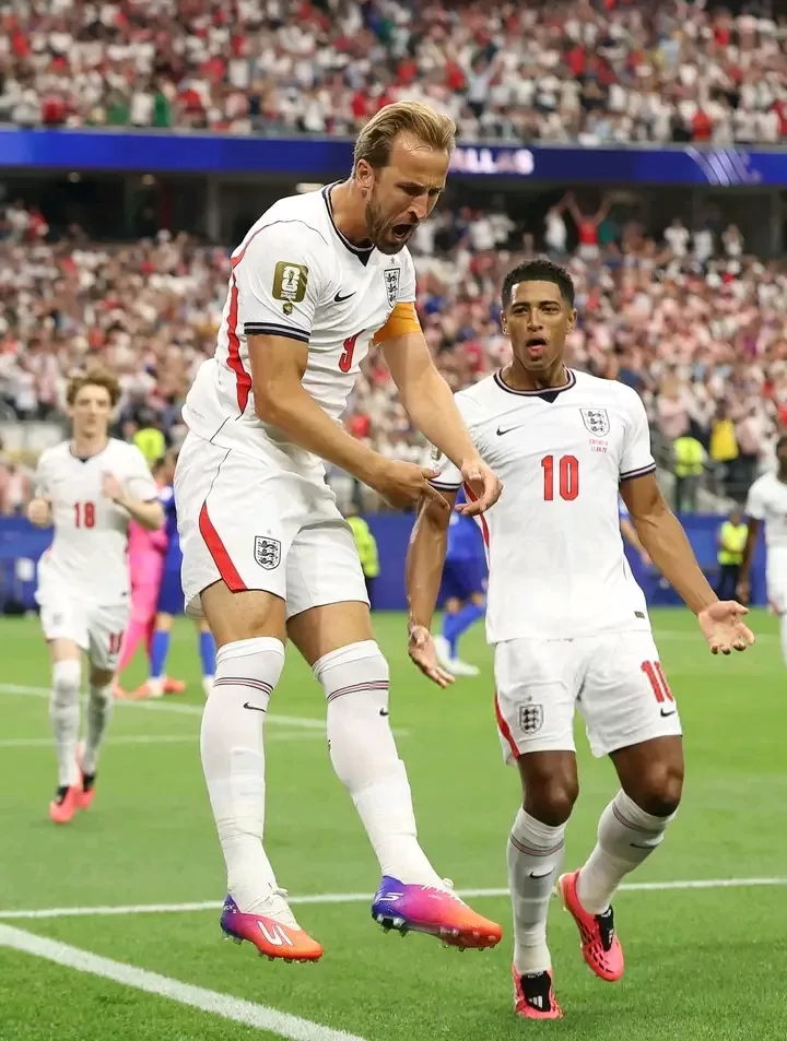 Deux footballeurs en tenue blanche célèbrent un but sur un terrain devant un public nombreux en tribunes