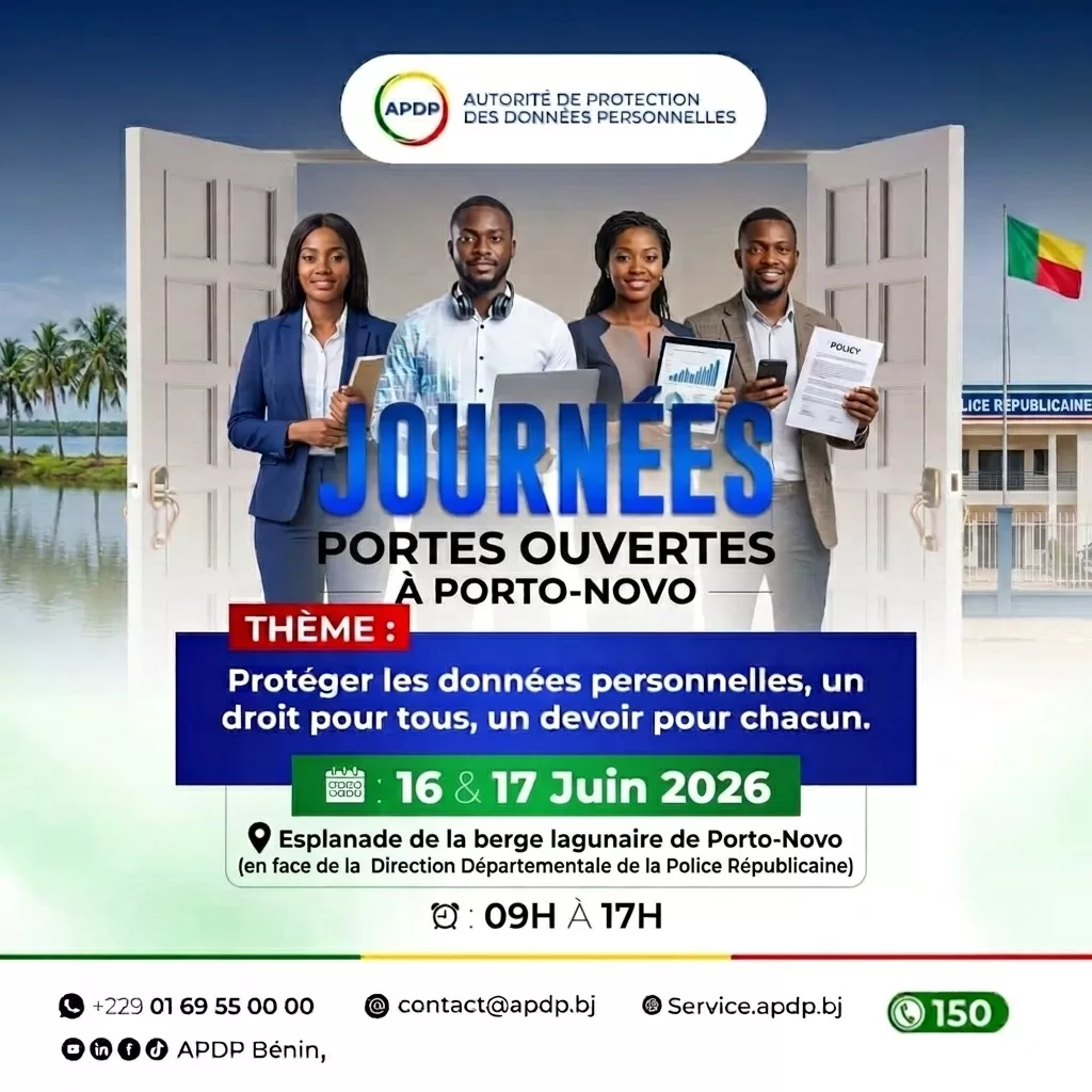 Quatre personnes debout souriant, chacune tenant un appareil ou document, sur fond d’une porte ouverte et d’un drapeau national