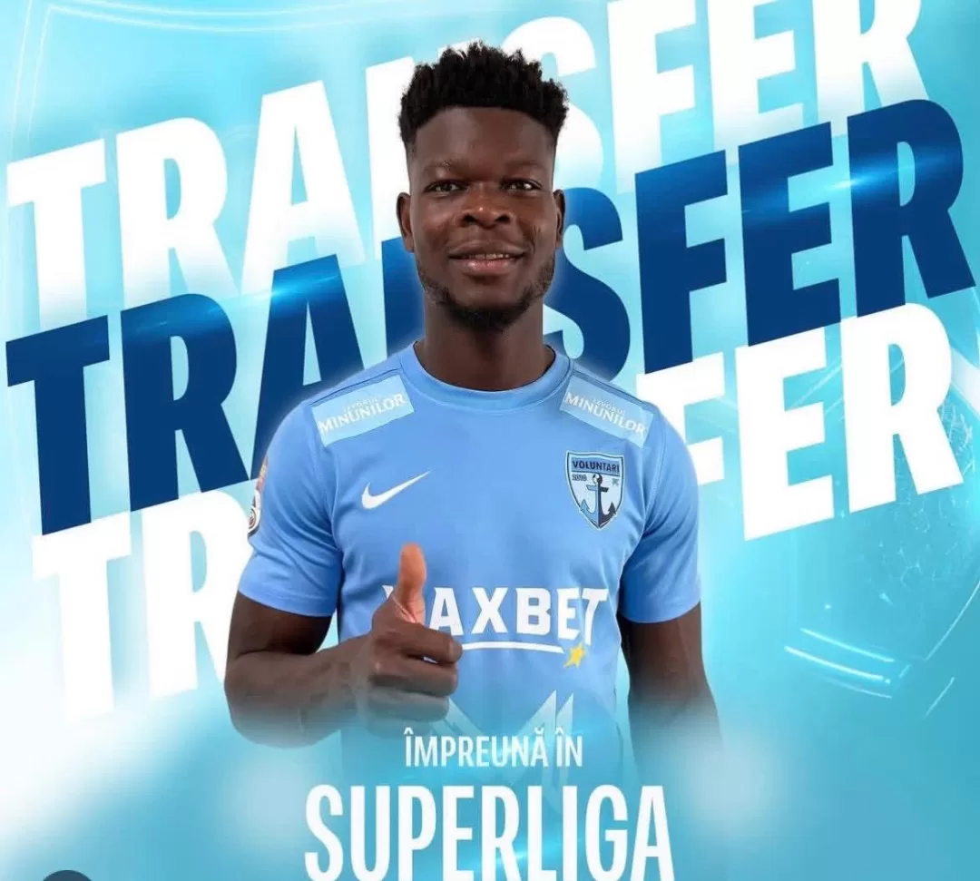 Homme en maillot de football bleu clair fait un pouce levé devant un fond marqué TRANSFER et SUPERLIGA