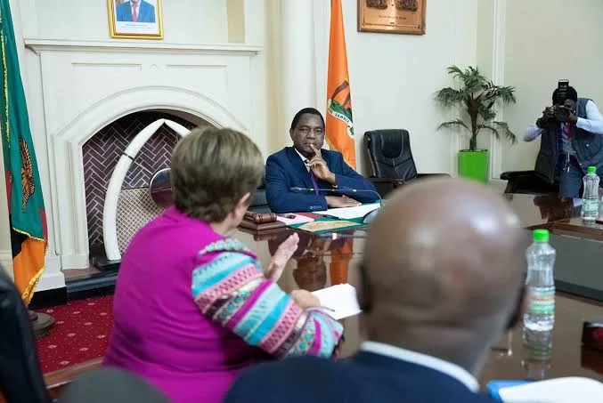 Plusieurs personnes sont assises autour d'une grande table en bois dans une salle avec un drapeau orange et un photographe en arrière-plan