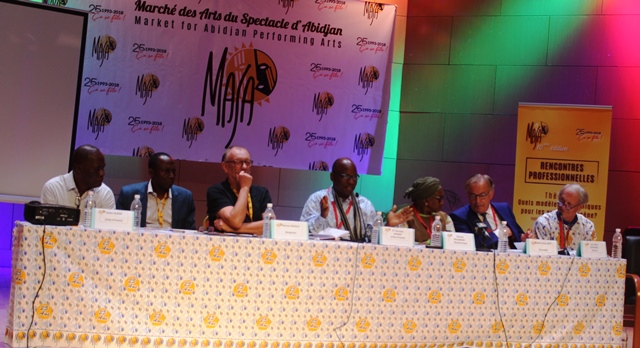 Sept personnes assises derrière une table de conférence, discutant lors d un événement sur une scène décorée du logo MASA et panneaux colorés
