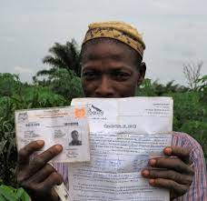 Un homme tenant une pièce d'identité et un document imprimé devant un paysage végétal.