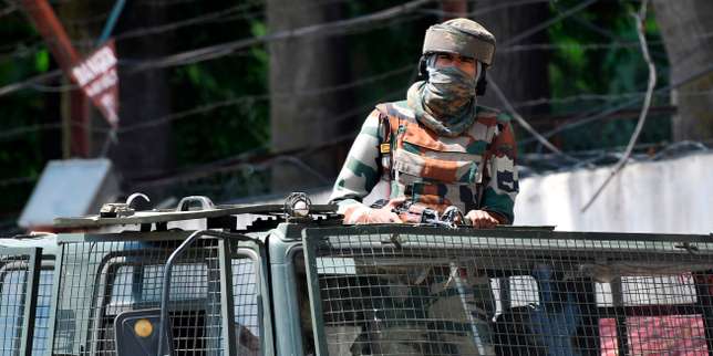Un soldat en tenue camouflée et visage couvert est posté dans un véhicule blindé équipé de grilles de protection