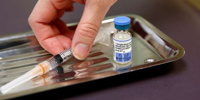 Une main manipule une seringue à côté d’un flacon de vaccin posé sur un plateau métallique.