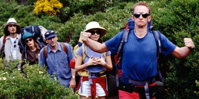 Un groupe de randonneurs en tenue d’été avancent en file indienne sur un sentier entouré de verdure dense