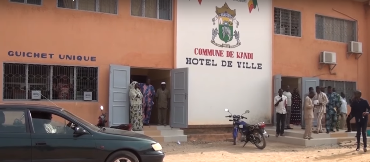 Façade d’un bâtiment communal avec plusieurs personnes devant et des véhicules garés à proximité