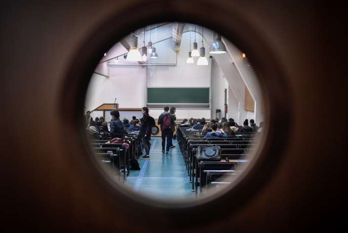 Salle de cours universitaire avec des étudiants assis et quelques-uns debout vus à travers un trou circulaire dans une porte