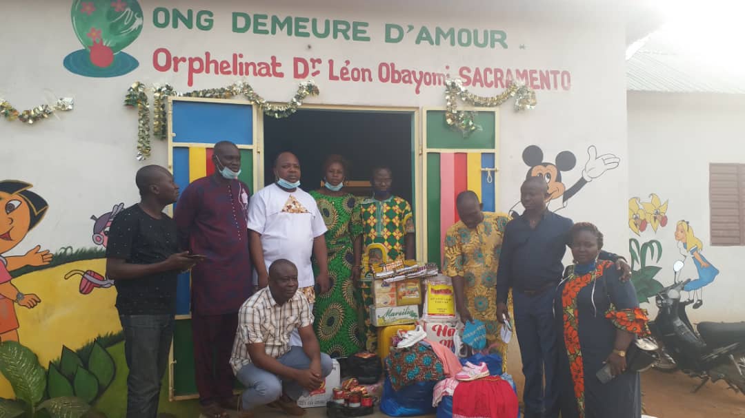Un groupe de personnes posant devant un bâtiment orphelinat avec des paquets de dons devant l'entrée décorée d'illustrations colorées