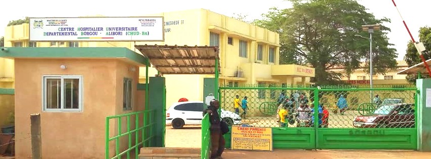 Entrée d un centre hospitalier avec portail vert et plusieurs personnes à l intérieur et à l’extérieur du site en journée