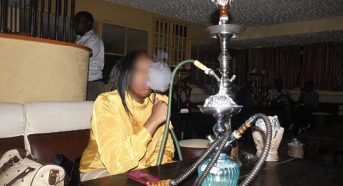 Une personne fumant une chicha dans un intérieur sombre avec plusieurs narguilés posés sur une table devant elle