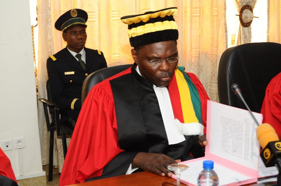 Homme en tenue judiciaire rouge et noire consulte un document ouvert lors d’une réunion officielle en intérieur
