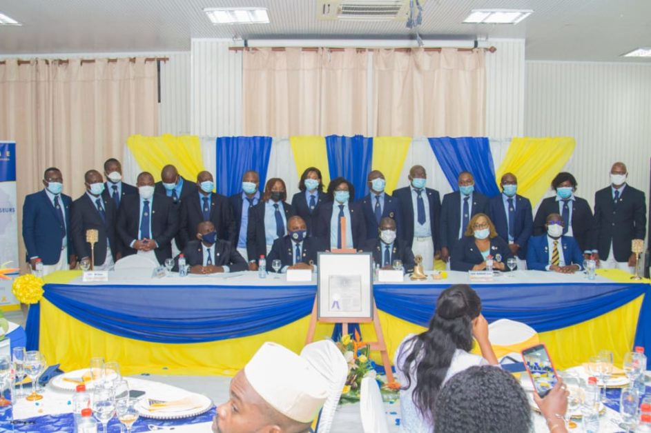 Un groupe de personnes en costume et masques pose derrière une table drapée de jaune et bleu lors d'une cérémonie officielle